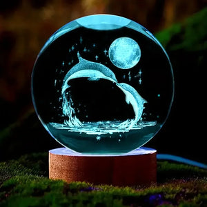 Veilleuse boule de cristal dauphin éclairée en bleu posée sur un socle en bois au cœur d'un décor naturel verdoyant