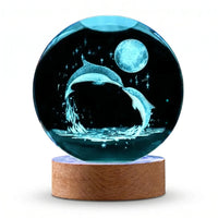 Boule de cristal avec gravure laser 3D de deux dauphins sautant sous la lune sur socle en bois sur fond blanc