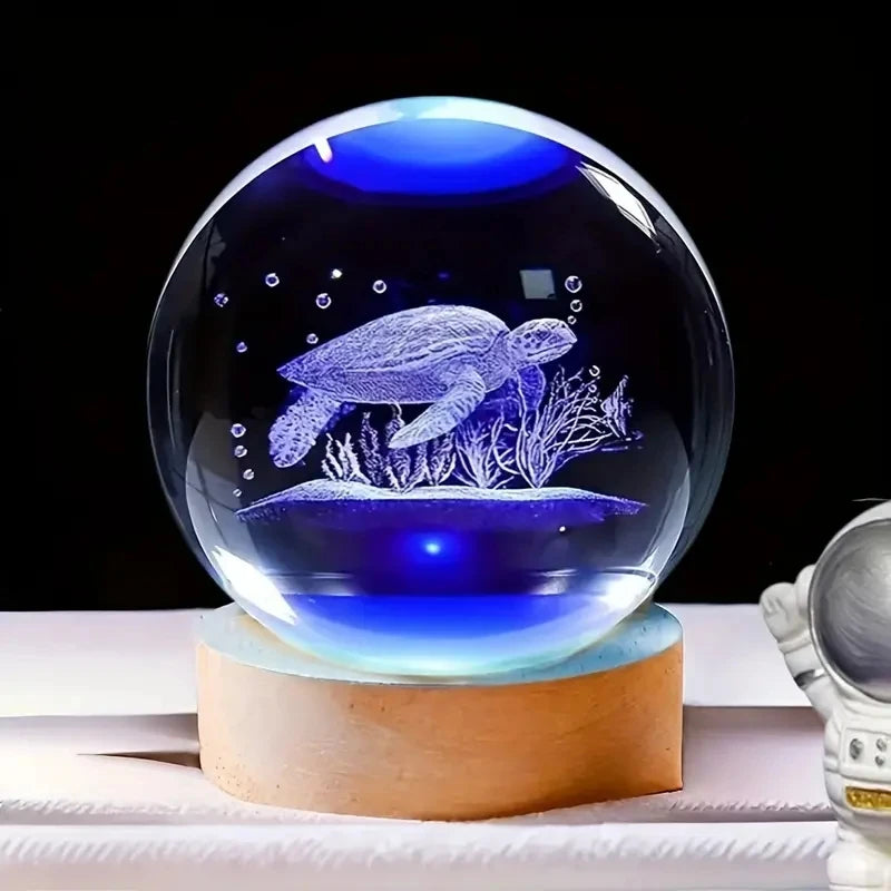 Boule de cristal gravée en 3d représentant une tortue marine éclairée par une lumière bleue sur socle en bois