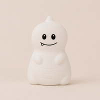 Veilleuse en silicone allumée en forme de petit dinosaure blanc, sur un fond beige neutre.