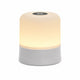 Lampe de chevet tactile au design cylindrique épuré, dotée d'une base grise et d'un diffuseur supérieur blanc allumé émettant une lueur chaude, avec un bouton de contrôle circulaire noir sur le dessus, présentée de face sur fond blanc.
