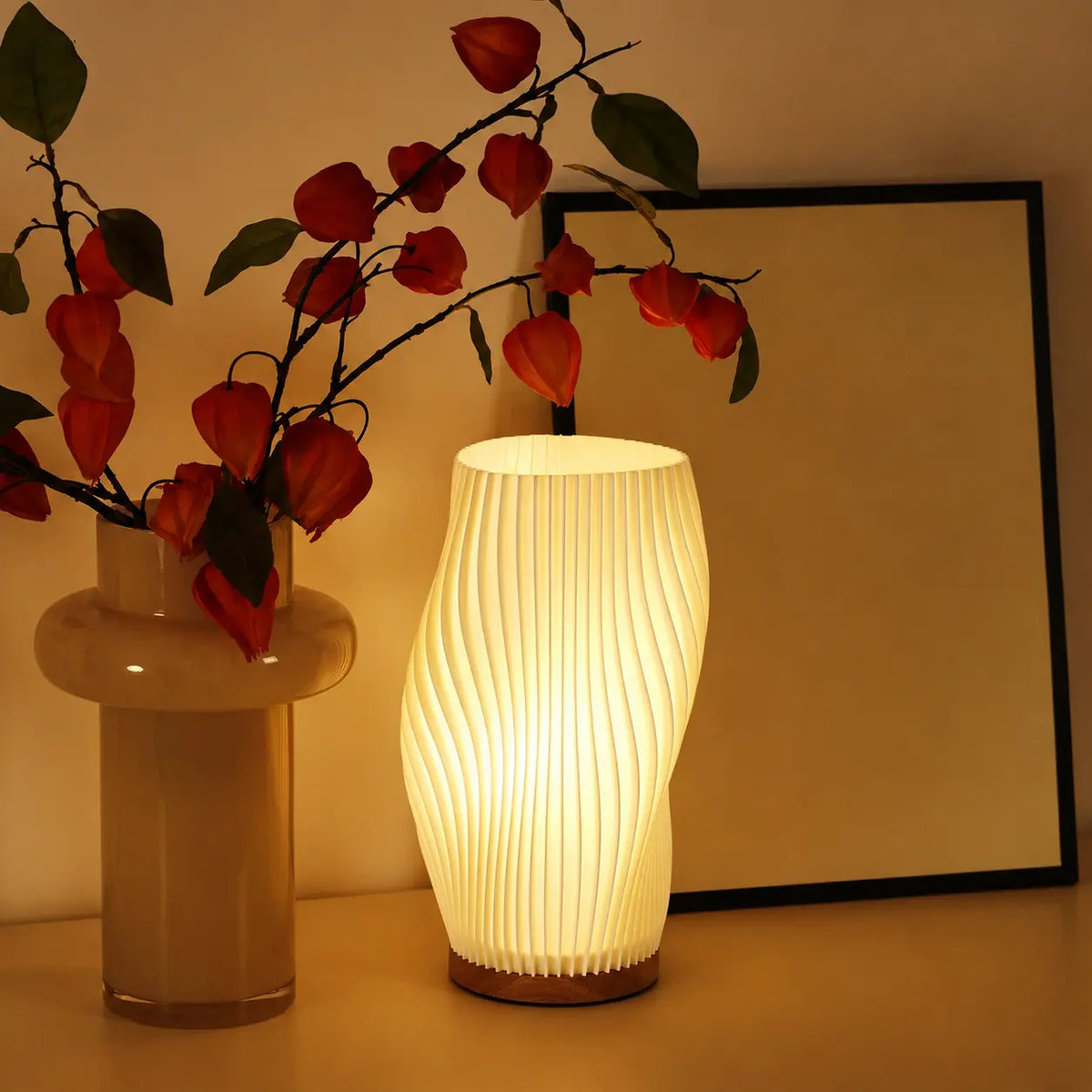 Lampe de table moderne ondulée allumée à côté d'un vase avec fleurs séchées et d'un cadre photo