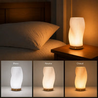 Lampe de table moderne ondulée posée sur une table de chevet et déclinée selon trois températures de couleur blanc neutre et chaud