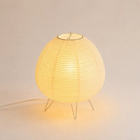 Lampe lanterne japonaise en papier de riz allumée sur un piétement fin en métal argenté.