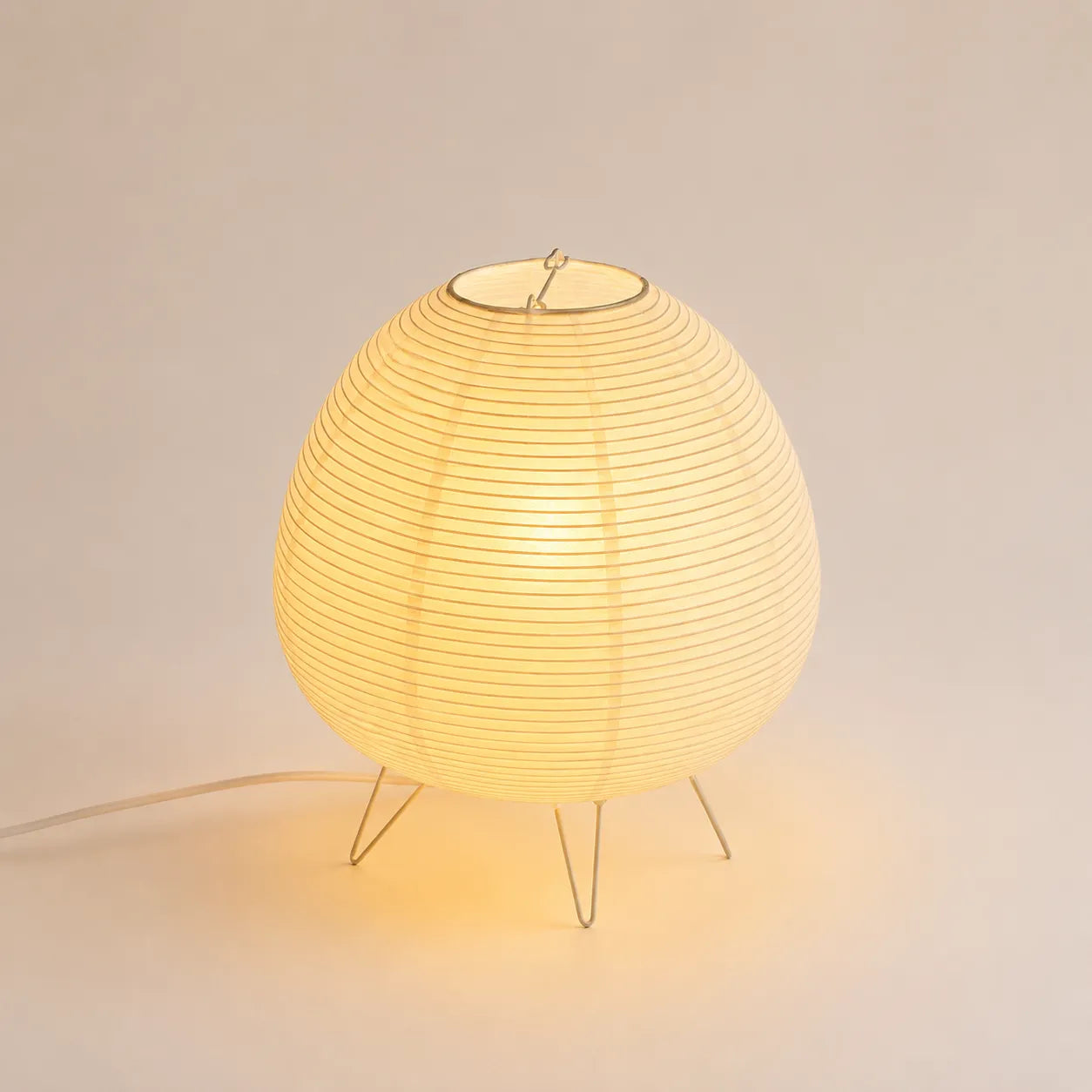 Lampe lanterne japonaise en papier de riz allumée sur un piétement fin en métal argenté.