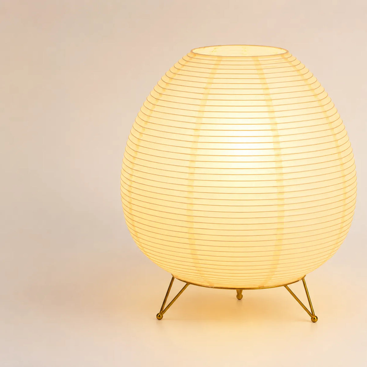 Lampe lanterne japonaise de forme ovale allumée sur son trépied en métal doré brillant.