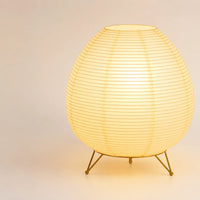 Lampe lanterne japonaise de forme ovale allumée sur son trépied en métal doré brillant.