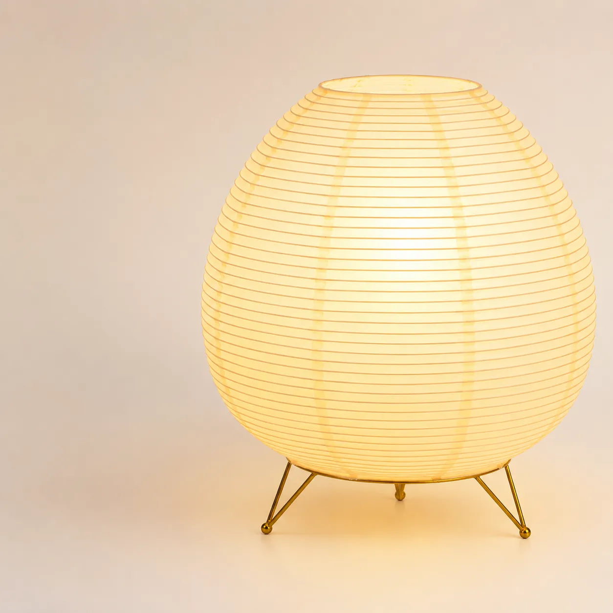 Lampe lanterne japonaise de forme ovale allumée sur son trépied en métal doré brillant.