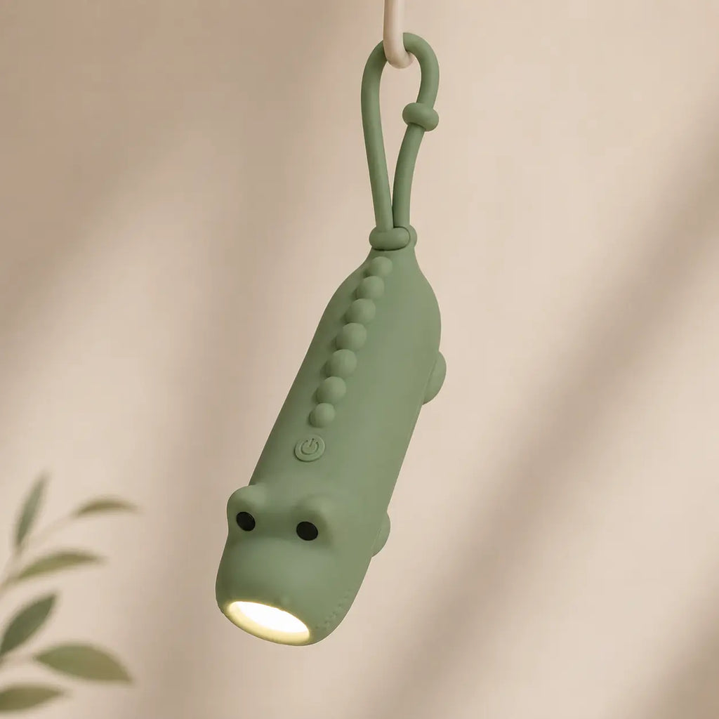 Lampe torche dinosaure verte suspendue par son attache en silicone, éclairant vers le bas.