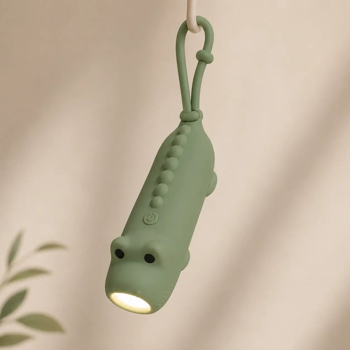 Lampe torche dinosaure verte suspendue par son attache en silicone, éclairant vers le bas.