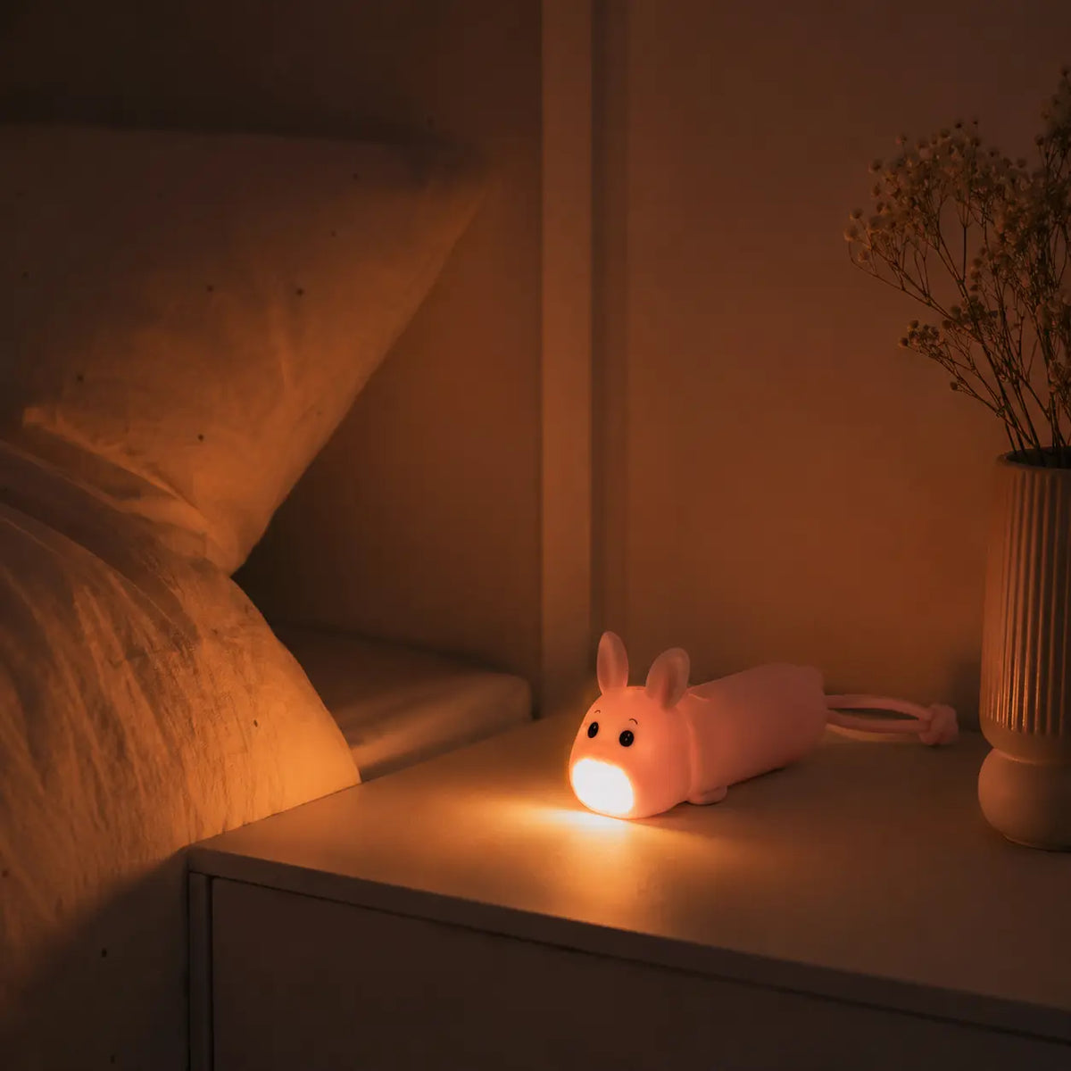 Lampe torche en forme de lapin rose éclairant une table de chevet dans l'obscurité.
