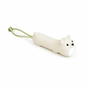 Lampe torche blanche en forme de petit ours allongé et allumé, posée à plat sur un fond blanc uni. Le corps cylindrique de la lampe dessine la silhouette de l'animal avec de petites pattes et une queue ronde, surmontée à l'extrémité par une tête d'ours aux petits yeux noirs et museau sombre. Une dragonne souple de couleur vert pastel est attachée à l'arrière, tandis que le faisceau lumineux se diffuse par la bouche de l'ours.