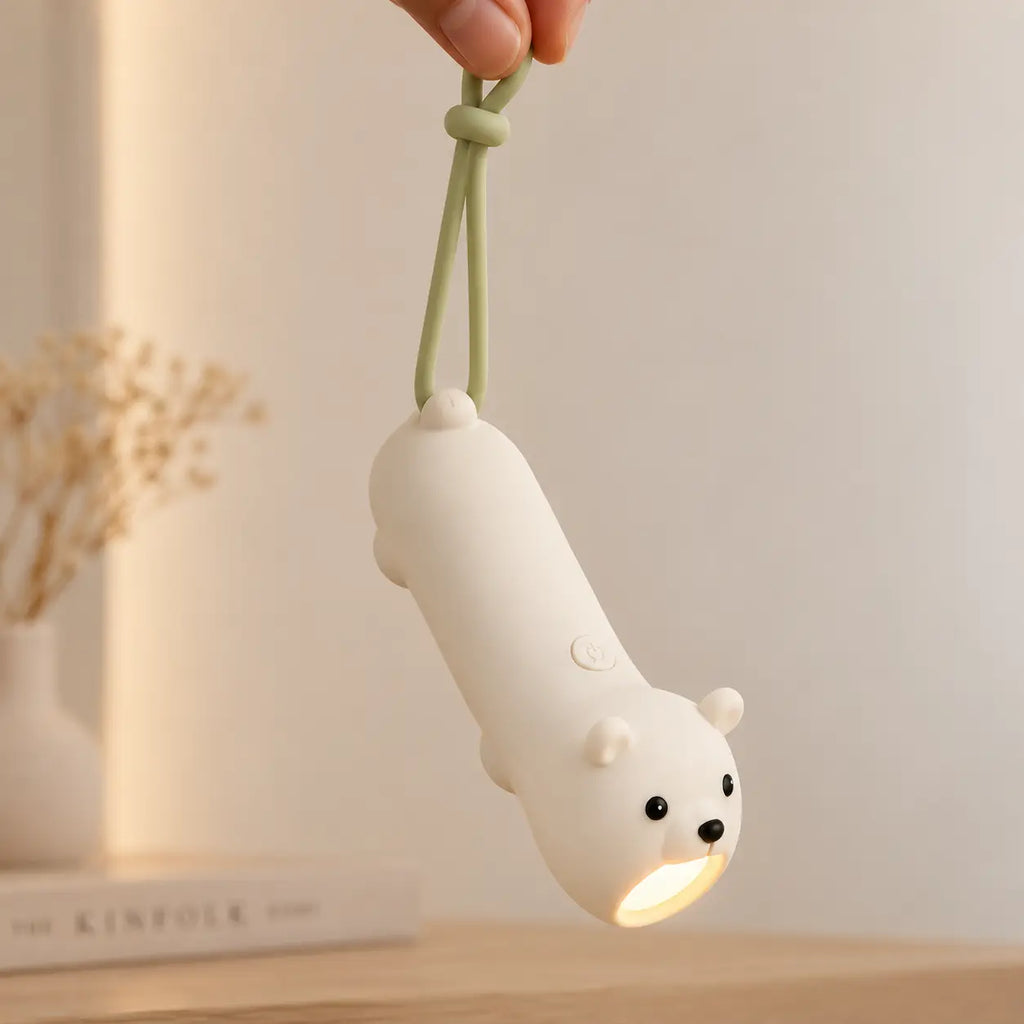 Lampe torche ours blanc allumée et suspendue par sa dragonne verte.