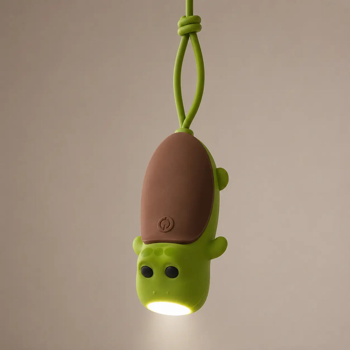 Lampe torche tortue verte suspendue par sa dragonne en silicone, éclairant vers le bas.