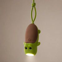 Lampe torche tortue verte suspendue par sa dragonne en silicone, éclairant vers le bas.
