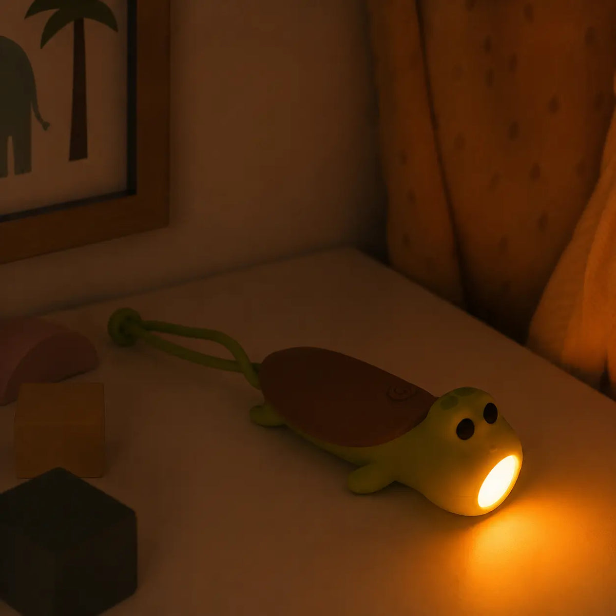 Lampe torche et veilleuse en forme de tortue verte posée sur une table de chevet, diffusant une lumière douce et rassurante pour la nuit.