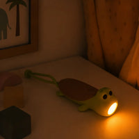 Lampe torche et veilleuse en forme de tortue verte posée sur une table de chevet, diffusant une lumière douce et rassurante pour la nuit.