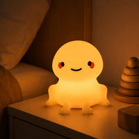 Petite veilleuse grenouille allumée diffusant une lumière chaude et douce sur une table de chevet dans une chambre d'enfant.