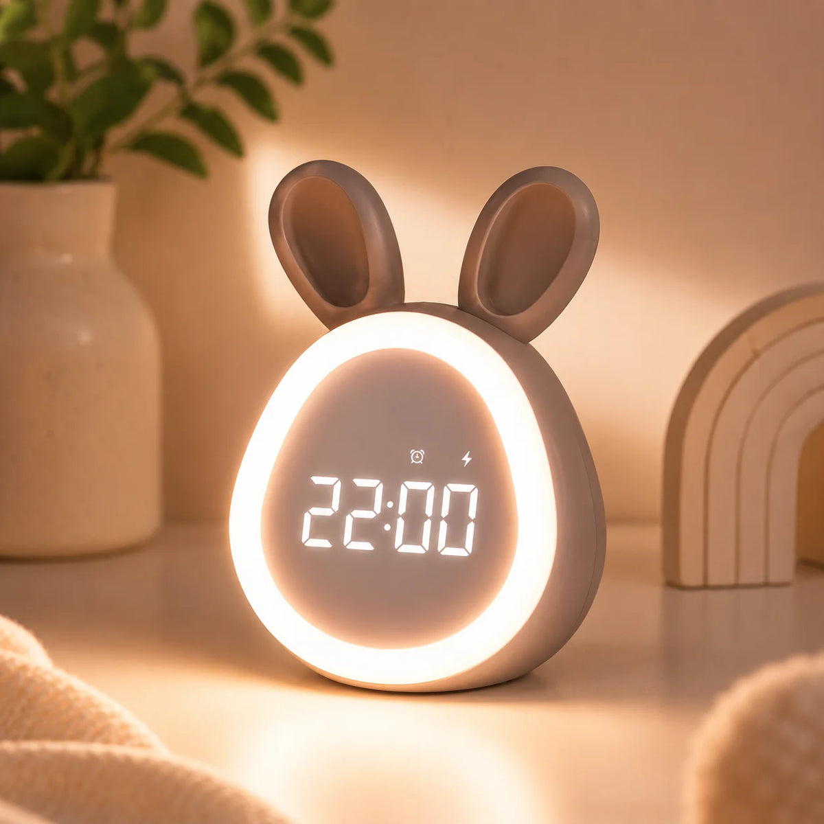 Réveil lapin LED blanc allumé diffusant une lumière chaude sur une table de chevet dans une ambiance tamisée.
