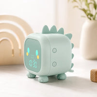Réveil veilleuse dinosaure vert vu de profil posé sur une table en bois claire avec un vase en arrière-plan.
