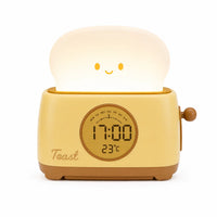 Réveil veilleuse en forme de grille-pain jaune crème avec une tranche de pain lumineuse et souriante, affichant l'heure et la température sur fond blanc.