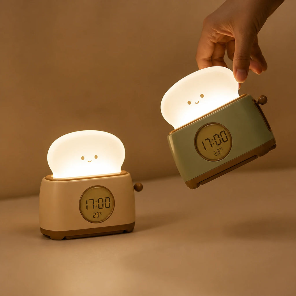 Deux réveils veilleuses grille-pain allumés, l'un jaune crème posé et l'un vert pastel tenu par une main dans une ambiance tamisée.