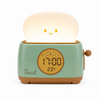 Réveil veilleuse en forme de grille-pain vert pastel avec sa tranche de pain lumineuse souriante sur fond blanc.