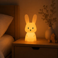 Veilleuse en forme de lapin allumée posée sur une table de chevet dans une ambiance chaleureuse.