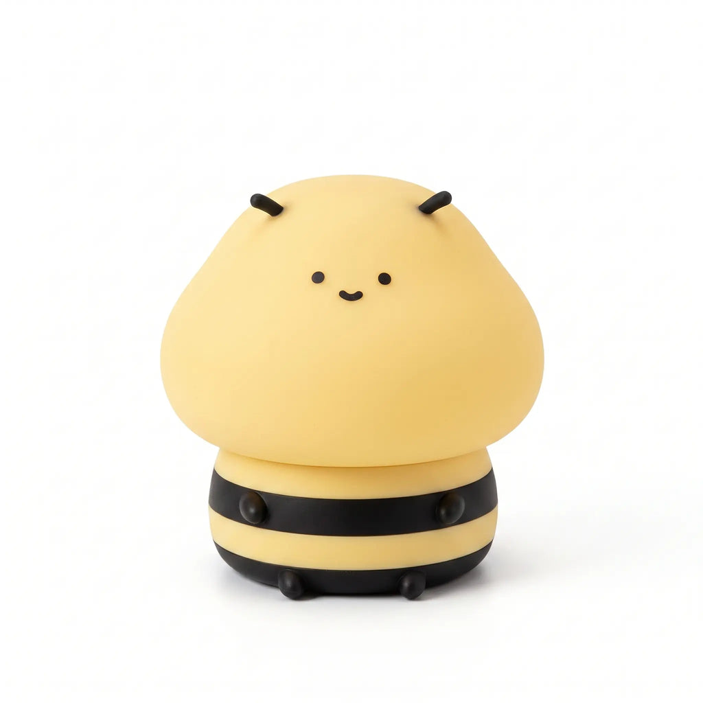 Veilleuse nomade en silicone souple en forme de petite abeille mignonne et souriante, allumée et diffusant une douce lueur jaune avec ses rayures noires caractéristiques, présentée de face sur fond blanc.