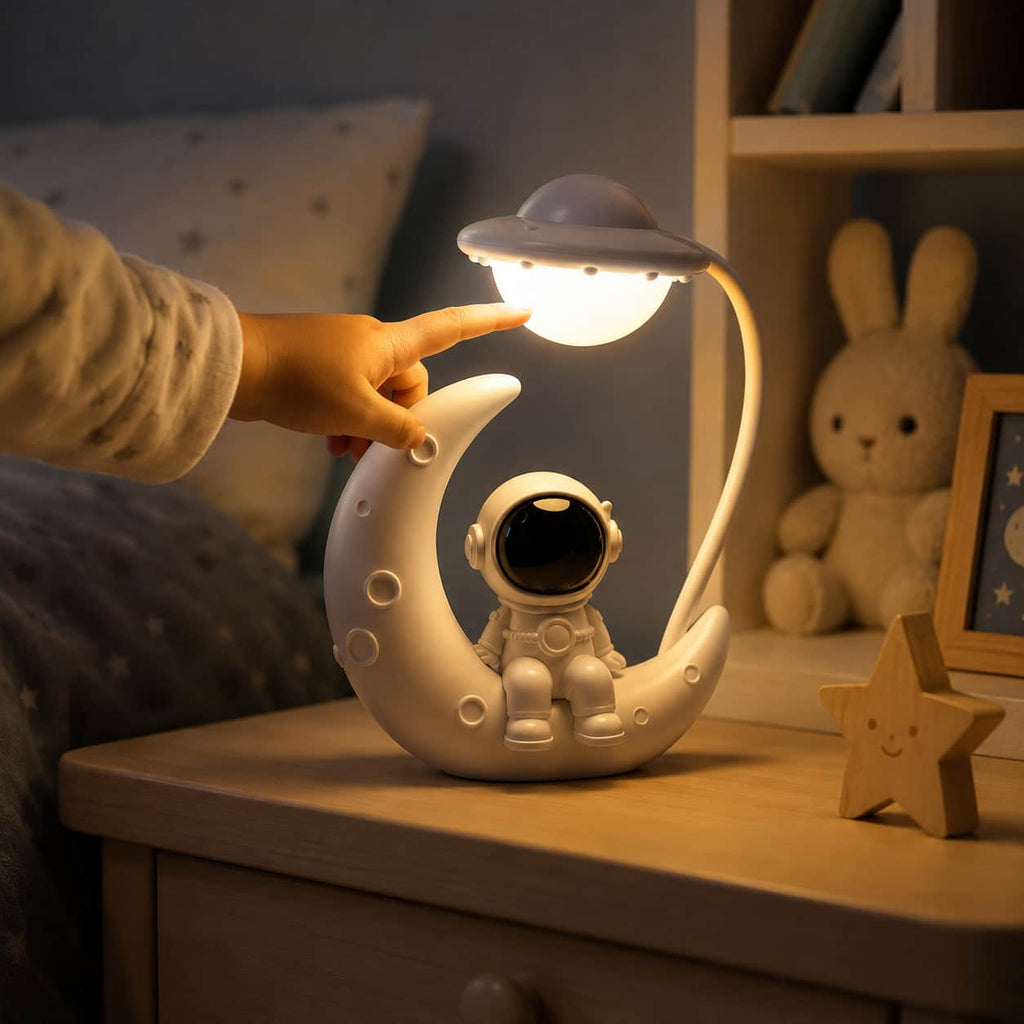 Veilleuse astronaute lune allumée sur une table de chevet avec la main d'un enfant qui touche la lampe, à côté d'une peluche lapin.