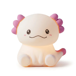 Veilleuse nomade en silicone souple en forme de petit axolotl mignon, allumée et diffusant une douce lueur chaude avec ses branchies et sa queue teintées de rose, présentée de face sur fond blanc.