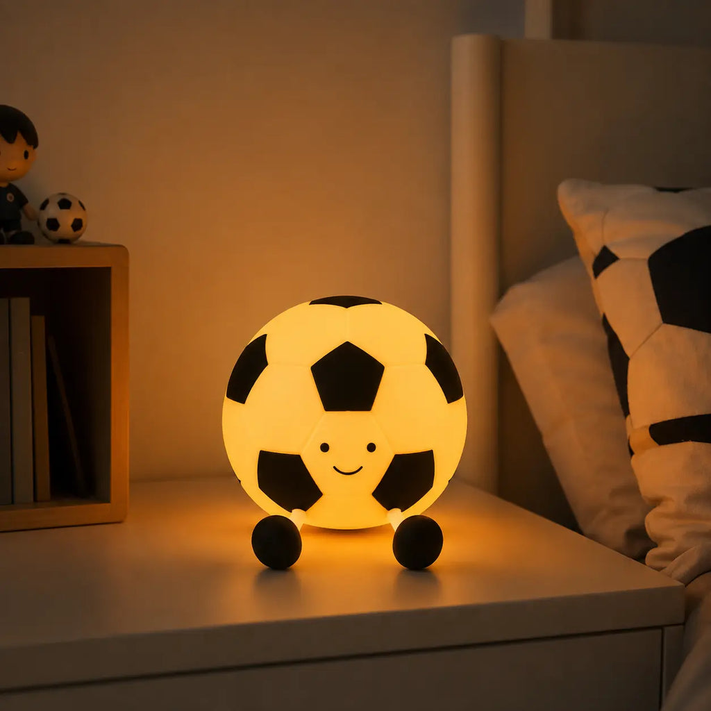 Veilleuse en forme de ballon de football souriant allumée avec lumière chaude sur une table de chevet