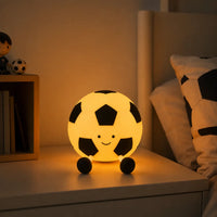 Veilleuse en forme de ballon de football souriant allumée avec lumière chaude sur une table de chevet
