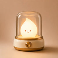 Veilleuse bougie LED coloris beige allumée diffusant une lumière chaude sous son dôme transparent.