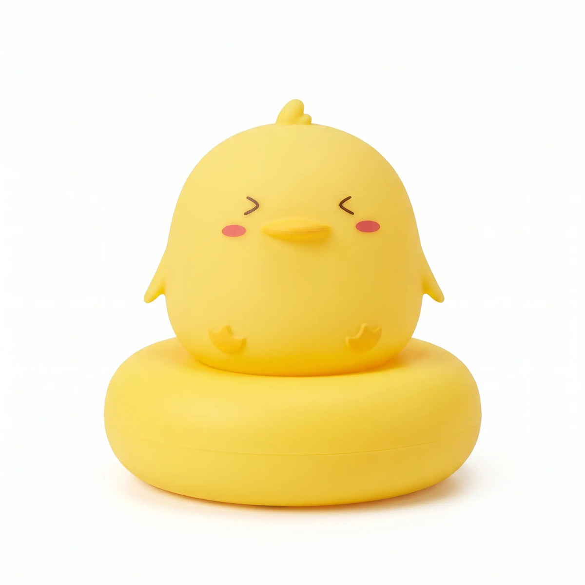 Veilleuse en forme de corps de petit canard jaune allumée, posée sur un large socle circulaire assorti sur fond blanc uni. Le personnage présente un aspect arrondi avec des yeux plissés de joie, un petit bec, des joues rosées, de petites ailes et pattes ainsi qu'une petite mèche sur la tête, diffusant une douce lueur chaleureuse.