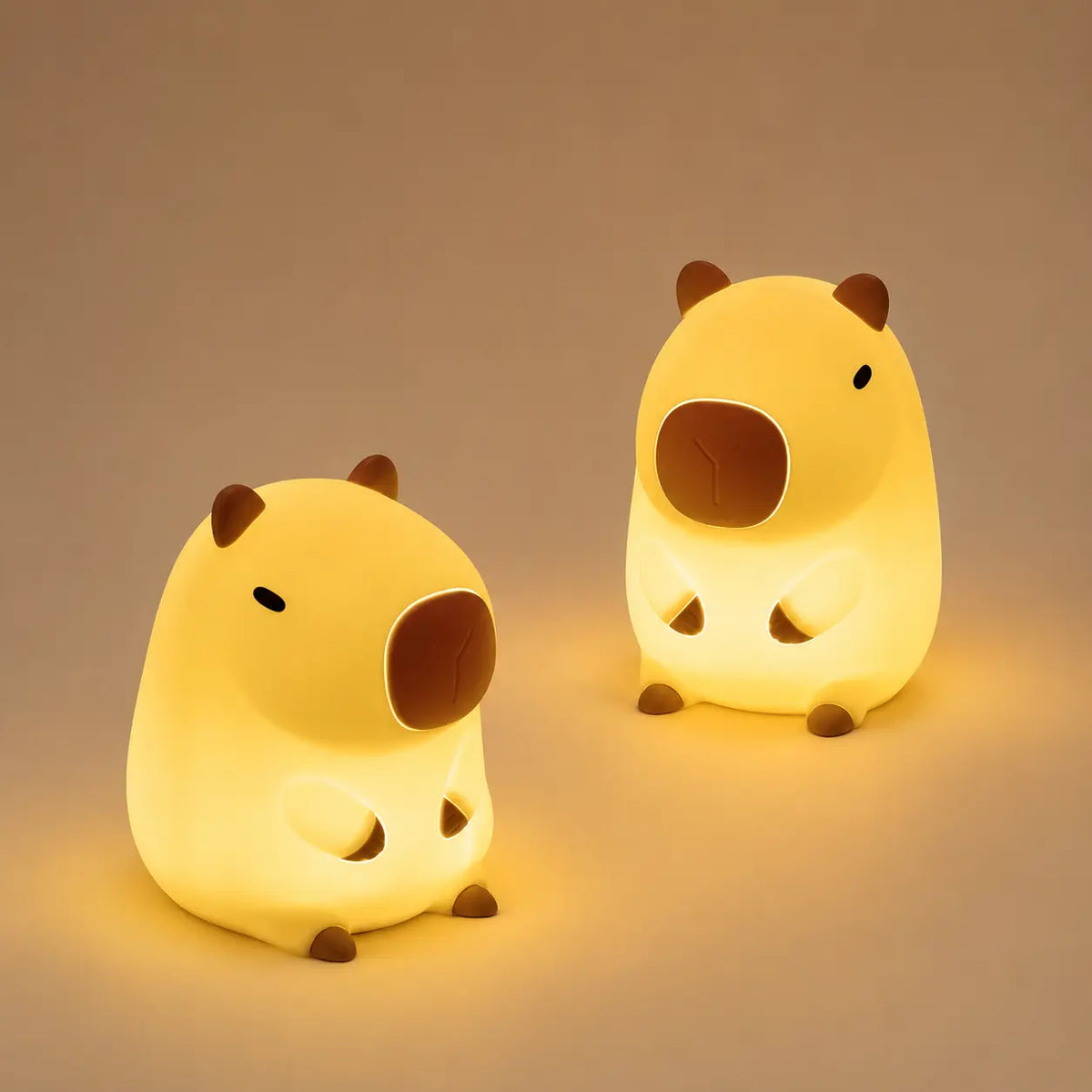 Deux veilleuses en silicone en forme de capybara illuminées côte à côte, mettant en valeur leur design mignon et leur lueur tamisée.