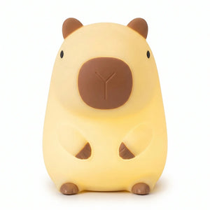 Veilleuse nomade en silicone souple en forme de capybara mignon assis, allumée et diffusant une douce lueur jaune chaleureuse, sur fond blanc.