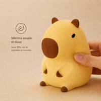 Main pressant doucement la veilleuse capybara pour illustrer sa texture en silicone souple, doux et sans BPA adapté aux enfants.