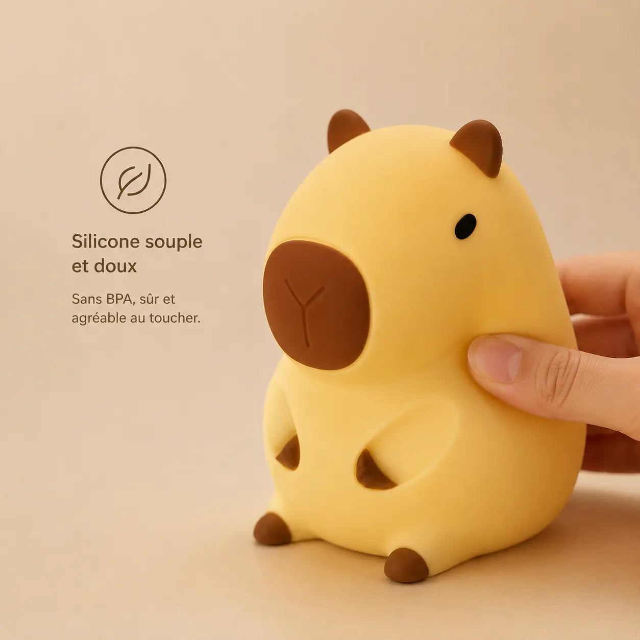 Main pressant doucement la veilleuse capybara pour illustrer sa texture en silicone souple, doux et sans BPA adapté aux enfants.