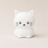 Veilleuse en silicone en forme de petit chat blanc, sur un fond beige neutre.