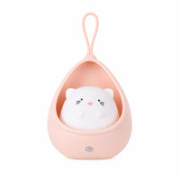 Veilleuse bébé éteinte représentant un petit chat blanc logé dans un cocon protecteur suspendu en silicone rose poudré, présentée de face sur fond blanc.