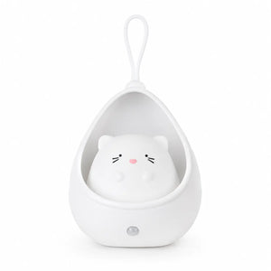 Veilleuse blanche en forme de petit chat mignon installé à l'intérieur d'un cocon protecteur en forme de goutte. La structure intègre une lanière en silicone sur le dessus pour être suspendue facilement et un capteur circulaire sur la base inférieure, présentée de face sur fond blanc.