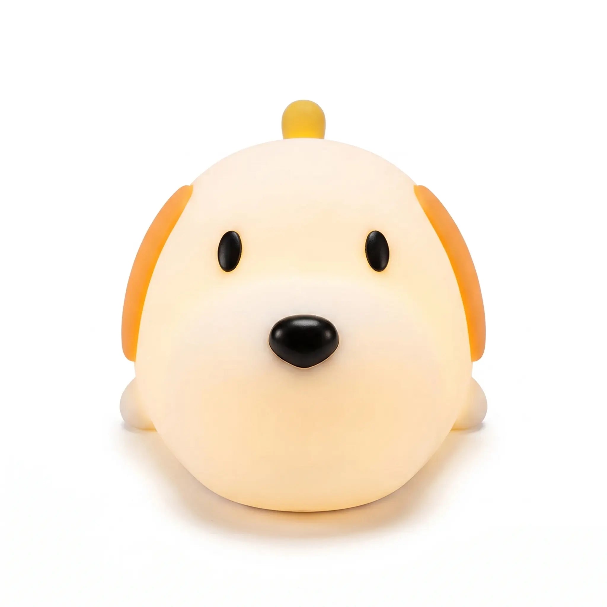 Veilleuse en silicone en forme de tête de petit chien mignon, allumée sur un fond blanc uni. Le personnage présente deux yeux noirs ovales, un nez noir arrondi, des oreilles tombantes orangées et une petite crête ou queue sur le dessus, diffusant une douce lueur chaude et tamisée.