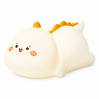 Veilleuse dinosaure tactile en silicone blanc avec de petites crêtes orange sur le dos et un visage mignon illuminé sur fond blanc.