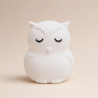 Veilleuse en silicone en forme de petit hibou blanc aux yeux fermés, sur un fond beige neutre.