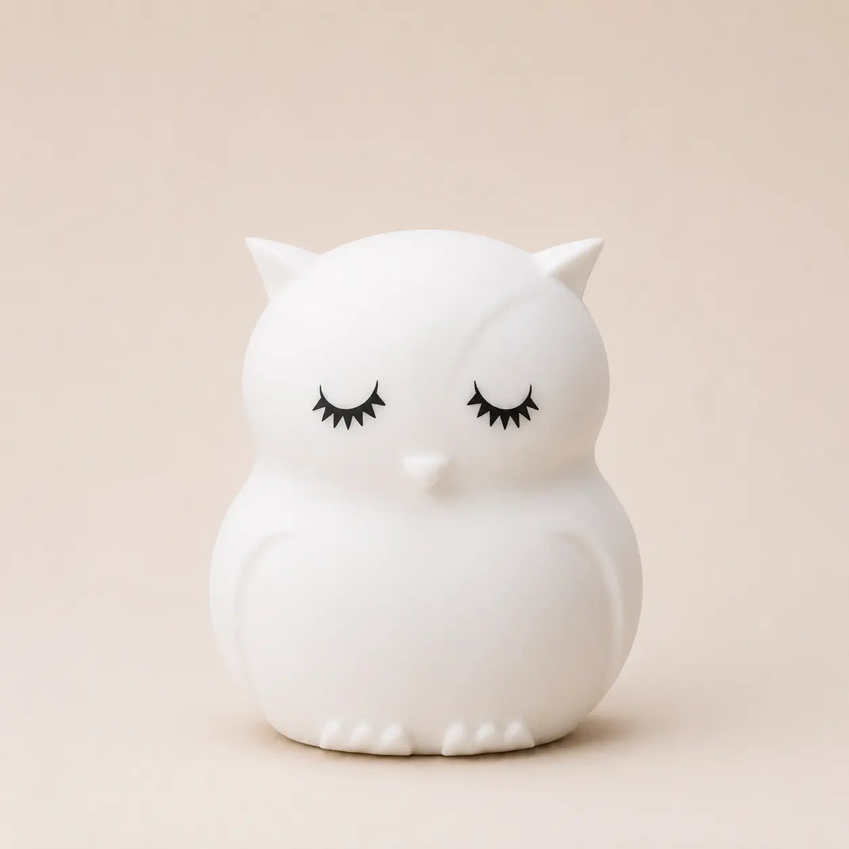 Veilleuse en silicone en forme de petit hibou blanc aux yeux fermés, sur un fond beige neutre.