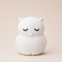 Veilleuse en silicone en forme de petit hibou blanc aux yeux fermés, sur un fond beige neutre.