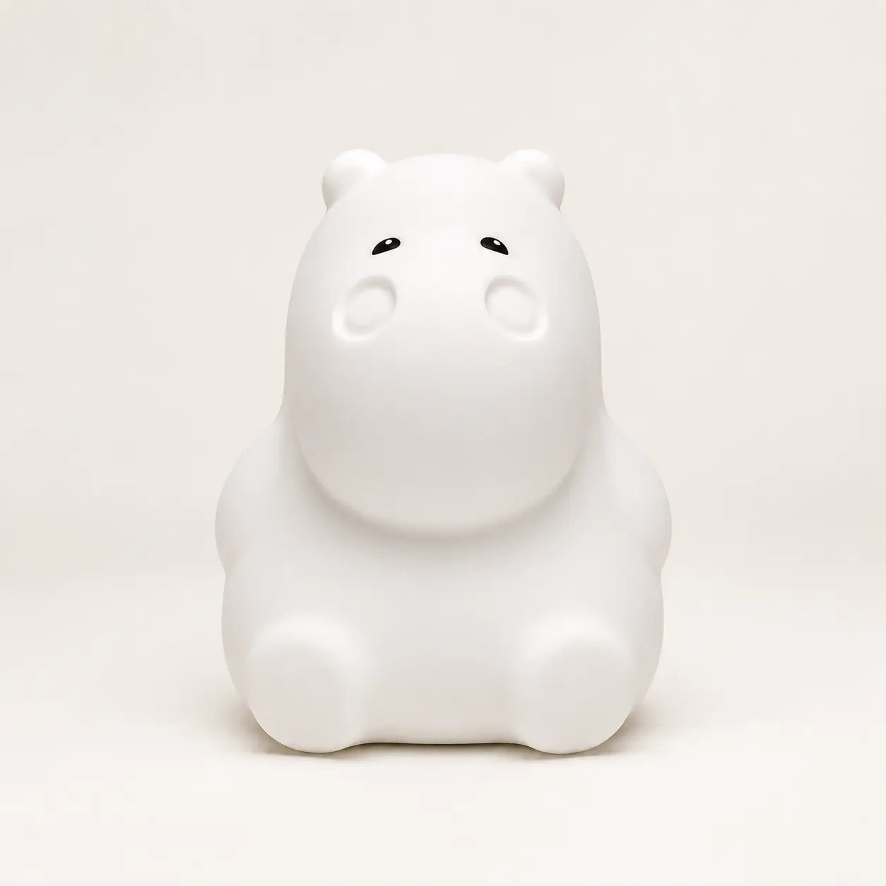 Veilleuse en silicone en forme de petit hippopotame blanc, sur un fond beige neutre.