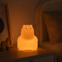 Veilleuse en forme de petit hippopotame allumée posée sur une table de chevet en bois dans une ambiance chaleureuse.