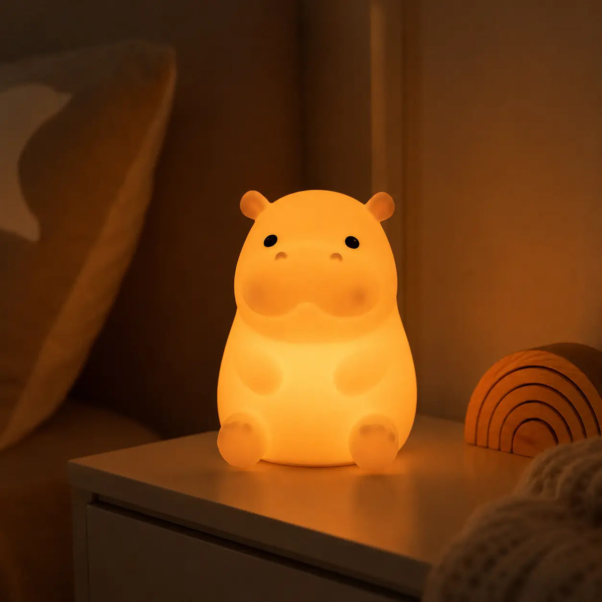Veilleuse hippopotame en silicone émettant une lumière chaude sur une table de chevet